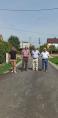 4 osoby, w tym Wójt Józef Piątek stoją na drodze asfaltowej. Po bokach zielona trawa, a w tle domy i słupy energetyczne